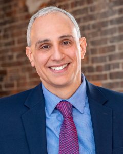 Picture of Steve Kottakis smiling in front of a brick wall